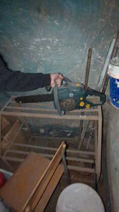 Рука Антона в подвале держит бензопилу